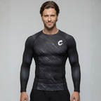 Man wearing a black long-sleeve BJJ rash guard with a logo on a gray background