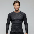 Man wearing a black long-sleeve athletic BJJ rash guard with a logo on a gray background