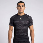 Man wearing a black athletic shirt with camouflage pattern on a white background